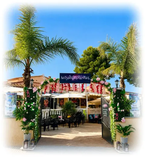 Entrada del Miami Lounge Bar con palmeras y arco de flores en Miami Platja