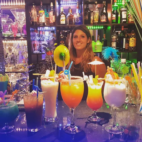 Camarera posando en la barra con una fila de cócteles tropicales de colores