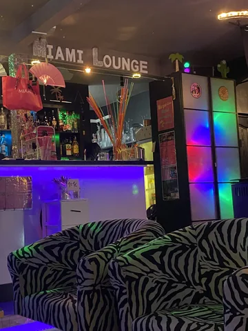 Interior con sofás de estampado cebra bajo el cartel Miami Lounge y luces de colores · Foto de un cliente en Google