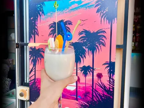 Piña colada frente al mural synthwave de palmeras del bar