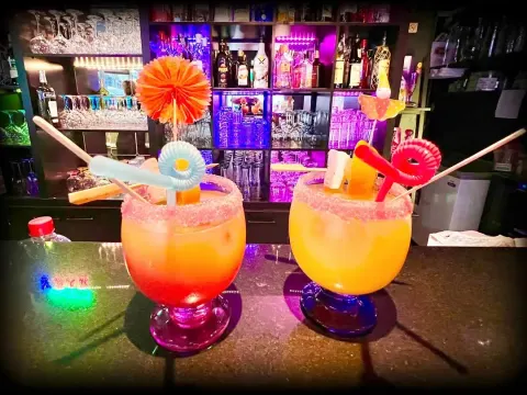 Dos cócteles naranjas decorados con piruletas y luces de colores